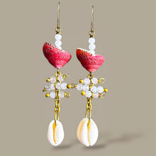 Load image into Gallery viewer, A pair of bohemian dangle earrings featuring pink coral heart-shaped beads, white shell beads, gold-toned metal links, and white cowrie shells, set against a solid taupe background.