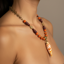 Load image into Gallery viewer, A close-up of a woman's neck and upper chest wearing a beaded necklace with orange and dark brown beads, gold-toned spacer details, and a large white and orange patterned shell pendant.