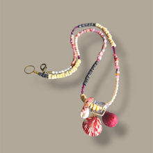 Load image into Gallery viewer, A beaded necklace featuring pastel pink, yellow, white, and purple beads, a clear glass block, and two shell charms including a red and white striped seashell and a textured pink seashell, set against a solid taupe background.