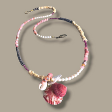 Load image into Gallery viewer, A handmade beaded necklace with pink, white, and dark gray beads, featuring a shell pendant and a small white flower charm, displayed on a solid taupe background.