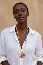 Load image into Gallery viewer, A woman wearing a white button-up shirt and a long beaded necklace with a pink shell pendant, photographed against a warm beige background.