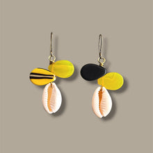 Load image into Gallery viewer, A pair of drop earrings featuring yellow and black disc-shaped beads, a white cowrie shell, and gold-tone hooks, displayed against a solid taupe background.