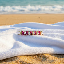 Load image into Gallery viewer, A brass hair barrettes embellished with faceted rubies and fresh water pearls sitting on a white beach towel on the sand. 