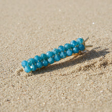 Load image into Gallery viewer, A brass hair barrettes embellished with faceted apatite sitting on the beach. 