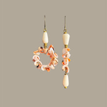 Load image into Gallery viewer, A pair of handmade asymmetrical dangle earrings featuring cream-colored stone beads and a circular cluster of peach, orange, and white shell, suspended from bras hooks against a solid taupe background.