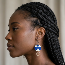 Load image into Gallery viewer, A close-up side profile of a woman with black braided hair wearing a dangling earring. The earring has a blue and white patterned top with a gold-tone circular charm and wire loop below.