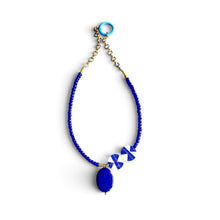 Load image into Gallery viewer, A beaded necklace featuring a vibrant blue braided cord, a large oval blue pendant, and two small blue-and-white patterned beads, finished with gold-tone chain links and a turquoise ring clasp, shown on a plain white background.