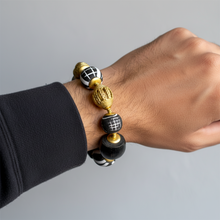 Load image into Gallery viewer, Hand wearing a bracelet with black, gold, and white beads on a gray background