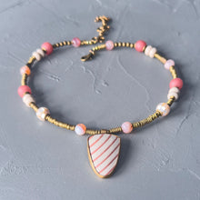 Load image into Gallery viewer, Necklace with pink and white beads and a striped pendant on a gray surface