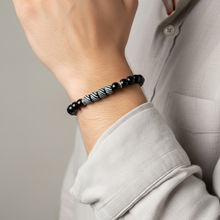 Load image into Gallery viewer, Person wearing a black and white beaded bracelet on a neutral background