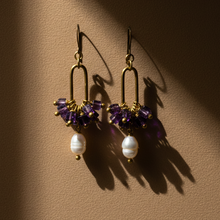 Load image into Gallery viewer, A pair of gold-colored metal earrings featuring purple amethyst cubes and white pearls arranged in a specific design.